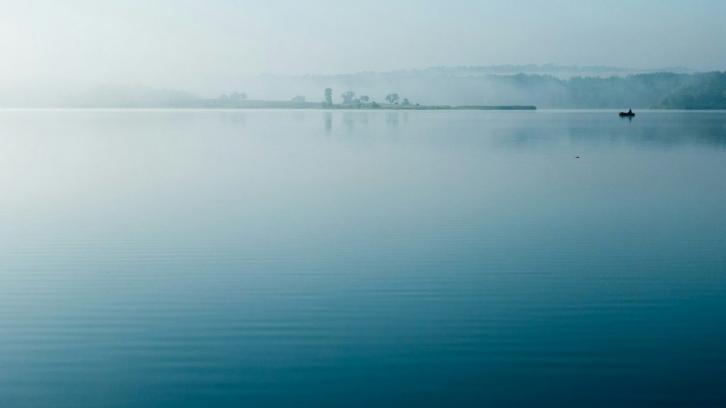 Ruhiger See im Morgennebel mit einzelnem Boot – Sinnbild für Abschied und Bestattung